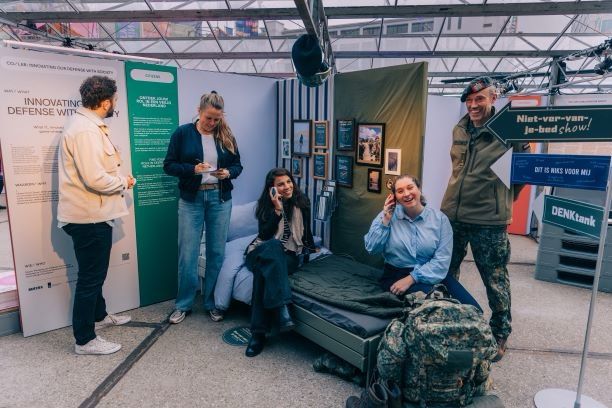 Burgerbreinen gezocht voor een innovatieve krijgsmacht

Hoe kunnen burgers bijdragen aan de veiligheid van Nederland? Die vraag stond deze week centraal op de Dutch Design Week in Eindhoven. Defensie liet geïnteresseerden daar zien hoe de organisatie met behulp van de civiele maatschappij kan vernieuwen.

Vanwege toenemende dreigingen moet Defensie steeds sneller innoveren. Dat lukt alleen als ook mensen van buiten Defensie met ideeën komen. Creatieve denkers, bedrijven en betrokken burgers kunnen zo helpen Nederland veiliger te maken. Om aansluiting met de samenleving te zoeken werkt Defensie samen met de Dutch Design Foundation en ontwerpstudio Muzus.

Tijdens de Dutch Design Week laat Muzus in de expositie ‘Designing Society’  verschillende experimenten zien. Deze gaan niet over het verzamelen van nieuwe ideeën. Wel gaan ze over het vinden van manieren om verbinding te maken tussen Defensie en de samenleving. Bezoekers luisterden bijvoorbeeld naar een fragment van een militair met zware bepakking in de hitte. Ze dachten mee over oplossingen om zijn omstandigheden te verlichten. Ook reageerden ze op een geschetste situatie in het geval van een grote stroomstoring. Daarbij werden ideeën geopperd over alternatieve vormen van onder meer stroom en voeding. Denk aan een knijpkat of het gezamenlijk aanschaffen van een generator, of aan eten bereiden zonder stroom of gas. Bezoekers stonden ook stil bij hoe en wat ze zelf kunnen bijdragen aan veiligheid. Denk aan programmeurs die willen helpen bij het ontwikkelen van algoritmen. Ook waren er mensen die zich in willen zetten voor goede voeding voor militairen. Ideeën zat dus om de boel aan te zwengelen.

Voorafgaand aan de expositie sprak Muzus ook al in verschillende Nederlandse steden met enkele honderden mensen op straat. De eerste resultaten laten zien waar de drempels en kansen liggen. Sommige bevraagden denken dat ze niet creatief genoeg zijn of te weinig weten van Defensie. Gesprekken over herkenbare dilemma’s helpen om de betrokkenheid te vergroten. Na de Dutch Design Week werkt Defensie verder aan een nieuw samenwerkingsconcept, gebaseerd op burgerparticipatie. De eerste versie daarvan wordt in februari 2026 verwacht. De Dutch Design Week duurt nog tot en met 26 oktober. Creatieve ideeën of oplossingen voor bepaalde dilemma’s? Stuur dan een mail naar kenniseninnovatie@mindef.nl

Bron: www.defensie.nl

[Alt-tekst in foto]

#defensie #dosco #clas #dcpl #werkenbijclas #koninklijkelandmacht #landmacht #werkenbijdefensie #buddybijdefensie #buddy #verbindingdienst #verbindelaar #defensieinclusief #diversiteit #inclusie